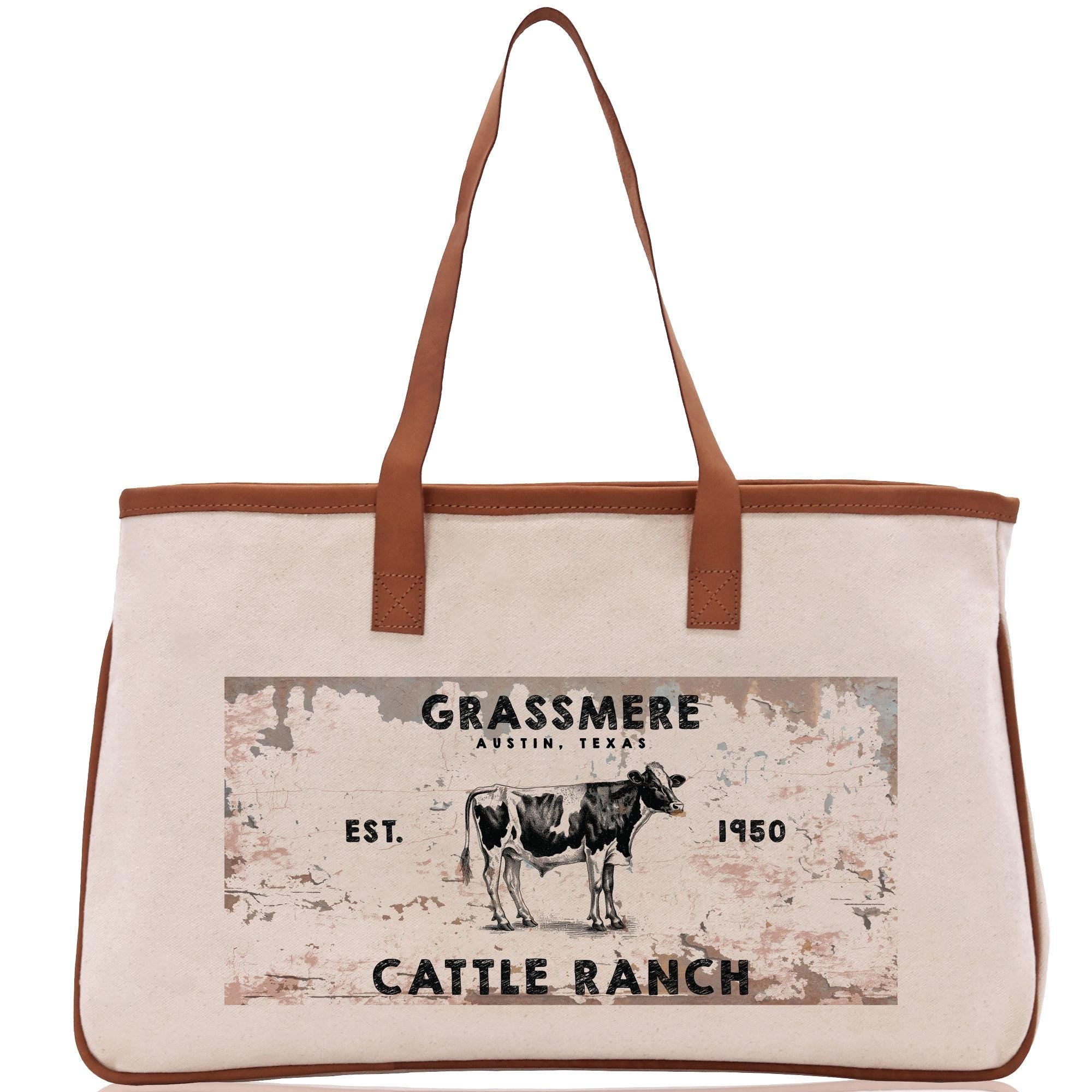 a beige canvas tote bag with a printed design on it, depicting a cow and the text &quot;Grassmere Austin, Texas&quot; and &quot;Cattle Ranch 1950&quot;.