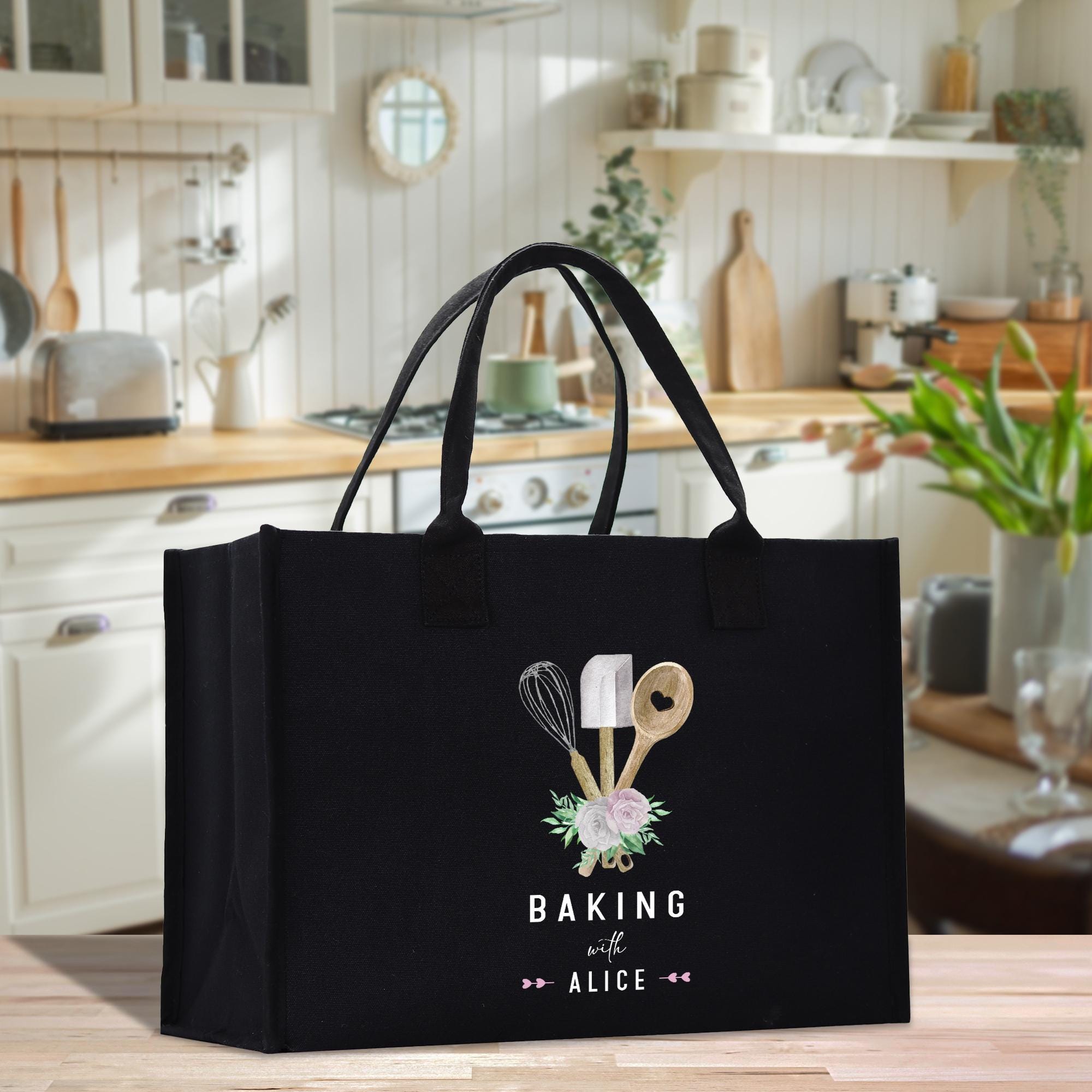 A black tote bag with a design of baking utensils and the text &quot;Baking with Alice&quot; printed on it, placed on a kitchen counter.