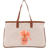 A tan tote bag with a brown handle and a bottle of perfume featuring orange flowers on top.