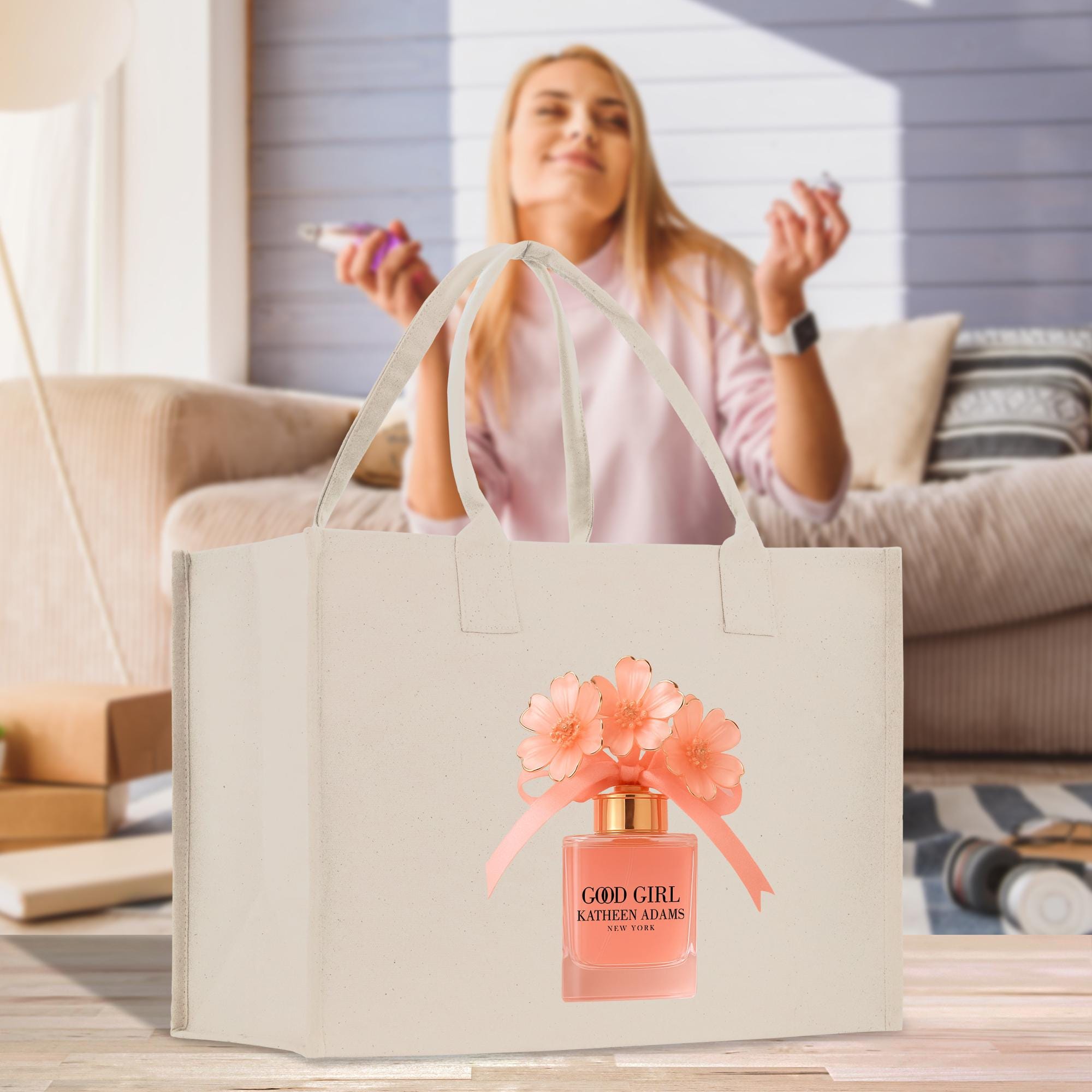 A woman is sitting on a couch in a living room, holding a phone and smiling. A beige tote bag with a perfume bottle design is placed on a wooden surface in front of her.