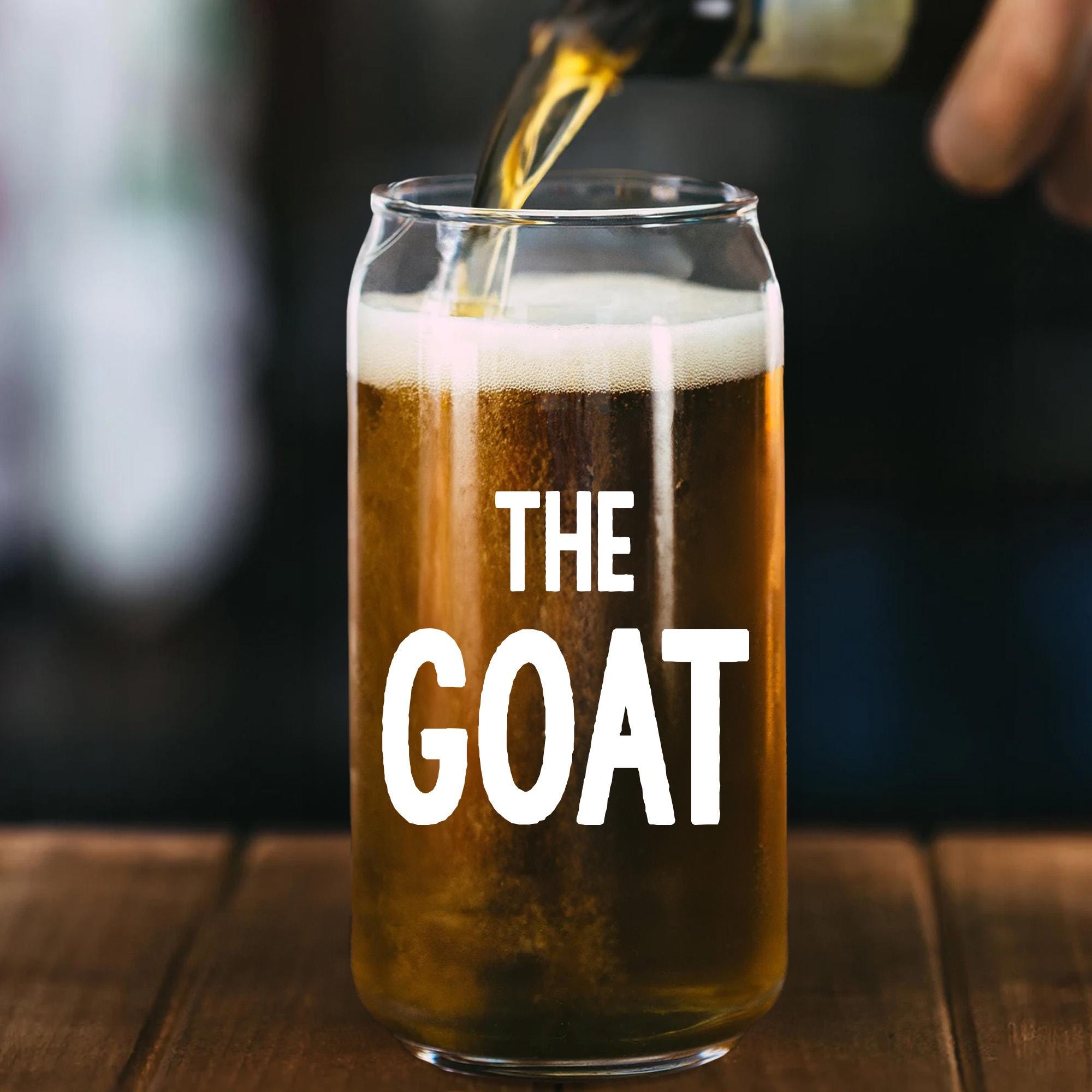 A glass of beer with a hand pouring liquid into it, with the text &quot;THE GOAT&quot; printed on the glass.