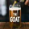 A glass of beer with a hand pouring liquid into it, with the text "THE GOAT" printed on the glass.