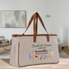 A beige canvas tote bag with a floral design and text printed on it, placed on a wooden surface.