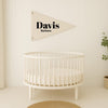 A white crib is positioned against a white wall, with a decorative triangle flag featuring the name "Barbara" hanging above it.