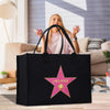 A black tote bag with a pink star logo and the name "Linda Perez" printed on it, placed on a wooden surface.