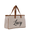 A beige canvas tote bag with the name "Lucy" printed on it in black cursive font.