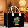A black tote bag with a Christmas-themed design, featuring a gingerbread man and other holiday-related elements, placed on a wooden surface.