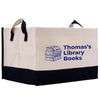 A beige tote bag with a black trim, featuring a graphic of a stack of books and the text "Thomas's Library Books" printed on it.