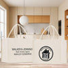 Two white tote bags with text and logos printed on them, placed on a wooden surface in a kitchen setting.