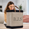 A woman is sitting on a couch in a living room, looking at a large tote bag with the initials "B.J.S." printed on it.