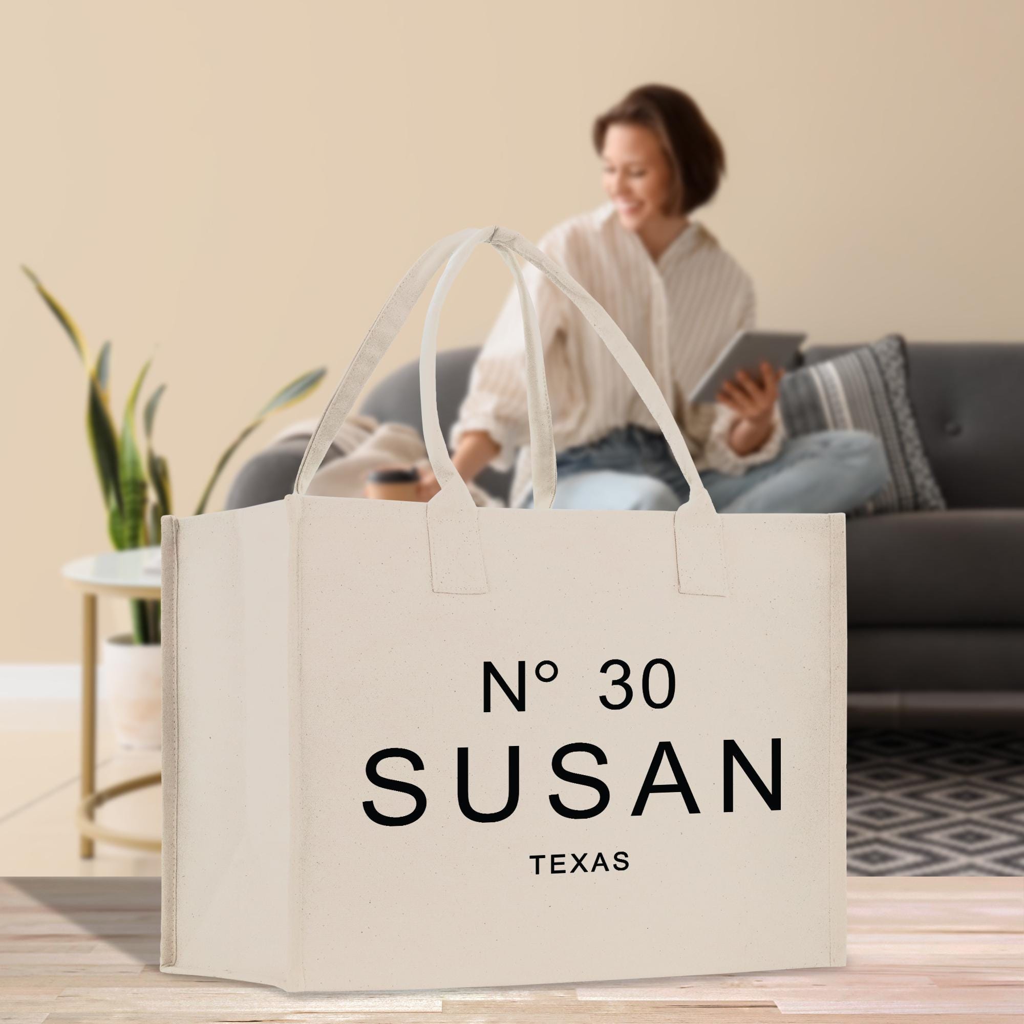 a large white tote bag with the text &quot;N° 30 SUSAN TEXAS&quot; printed on it, placed on a wooden floor in a living room setting.
