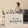 a large white tote bag with the text "N° 30 SUSAN TEXAS" printed on it, placed on a wooden floor in a living room setting.