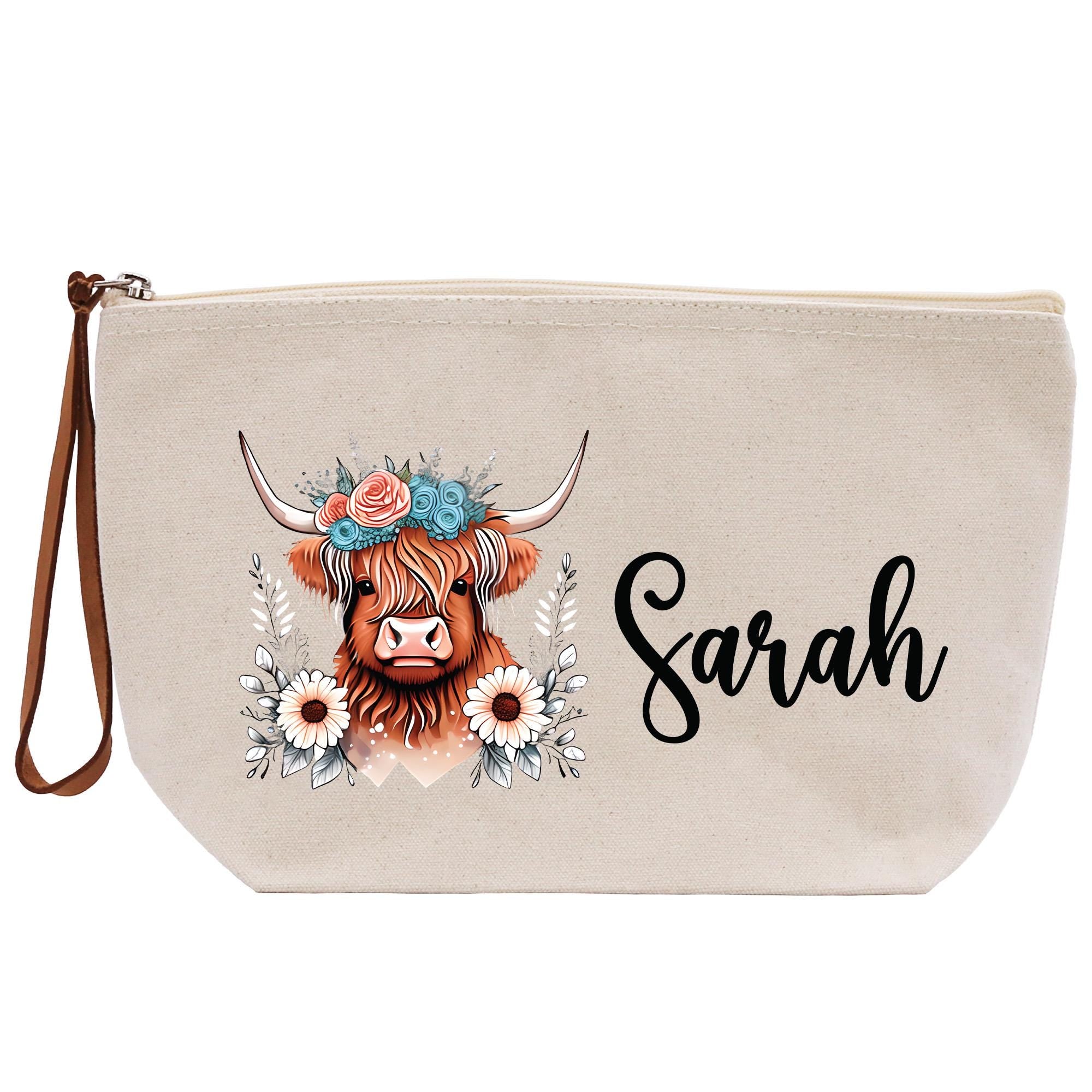 A beige canvas bag with a printed design of a cow&#39;s head wearing a floral crown and surrounded by flowers. The name &quot;Sarah&quot; is written in cursive below the cow&#39;s head.