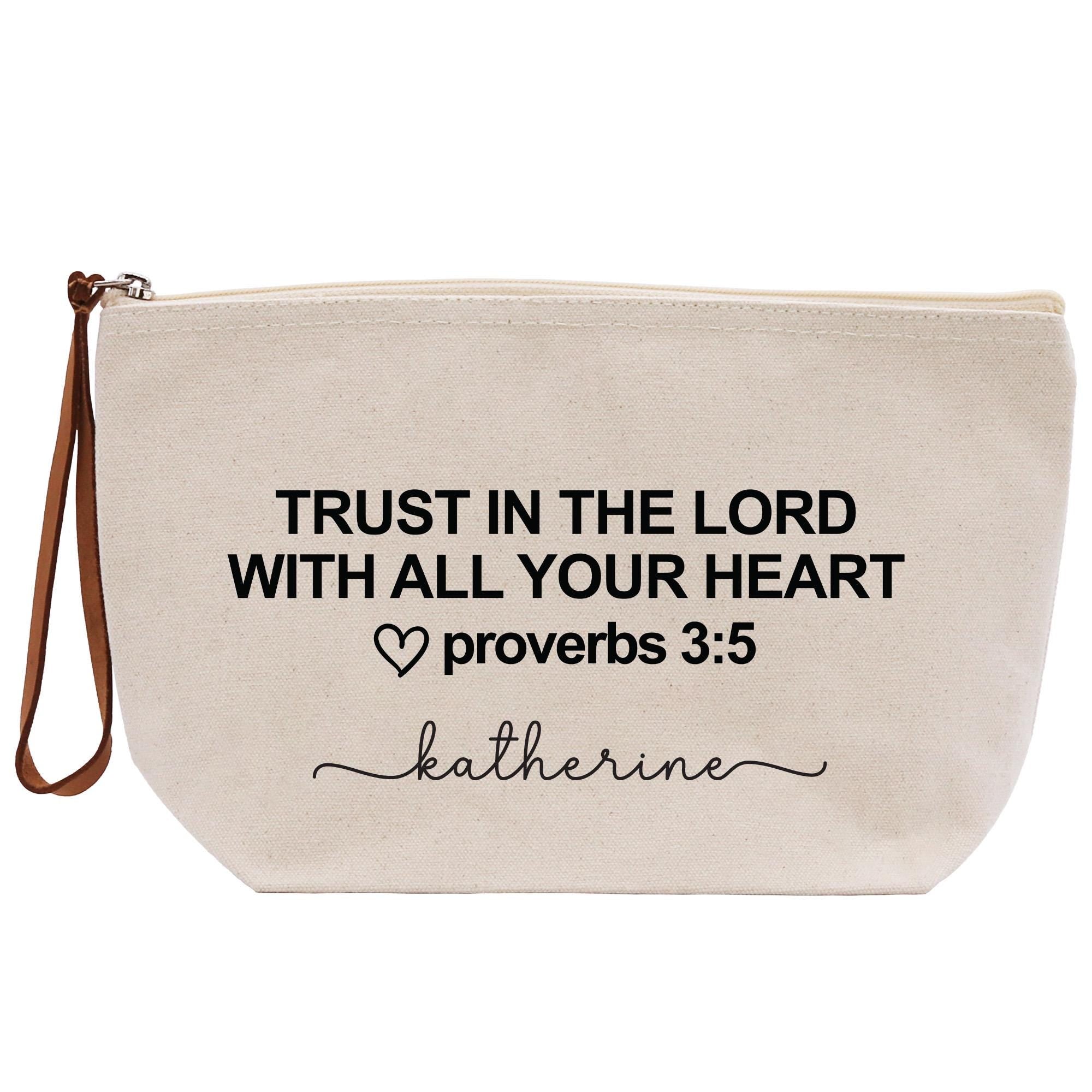 A beige canvas tote bag with the text &quot;TRUST IN THE LORD WITH ALL YOUR HEART&quot; printed on it, along with a heart symbol and the Bible verse &quot;proverbs 3:5&quot; below it.
