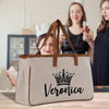 A large beige tote bag with the name "Veronica" printed on it, along with a crown design, is displayed in the foreground. In the background, two women are seen enjoying drinks and socializing.