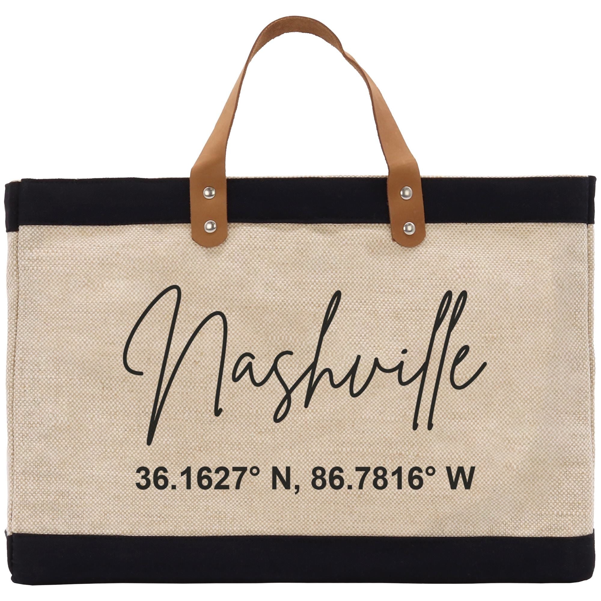 A beige tote bag with black trim and a leather handle, featuring the text &quot;Nashville&quot; and a coordinate pair &quot;36.1627° N, 86.7816° W&quot; printed on it.