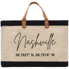 A beige tote bag with black trim and a leather handle, featuring the text "Nashville" and a coordinate pair "36.1627° N, 86.7816° W" printed on it.