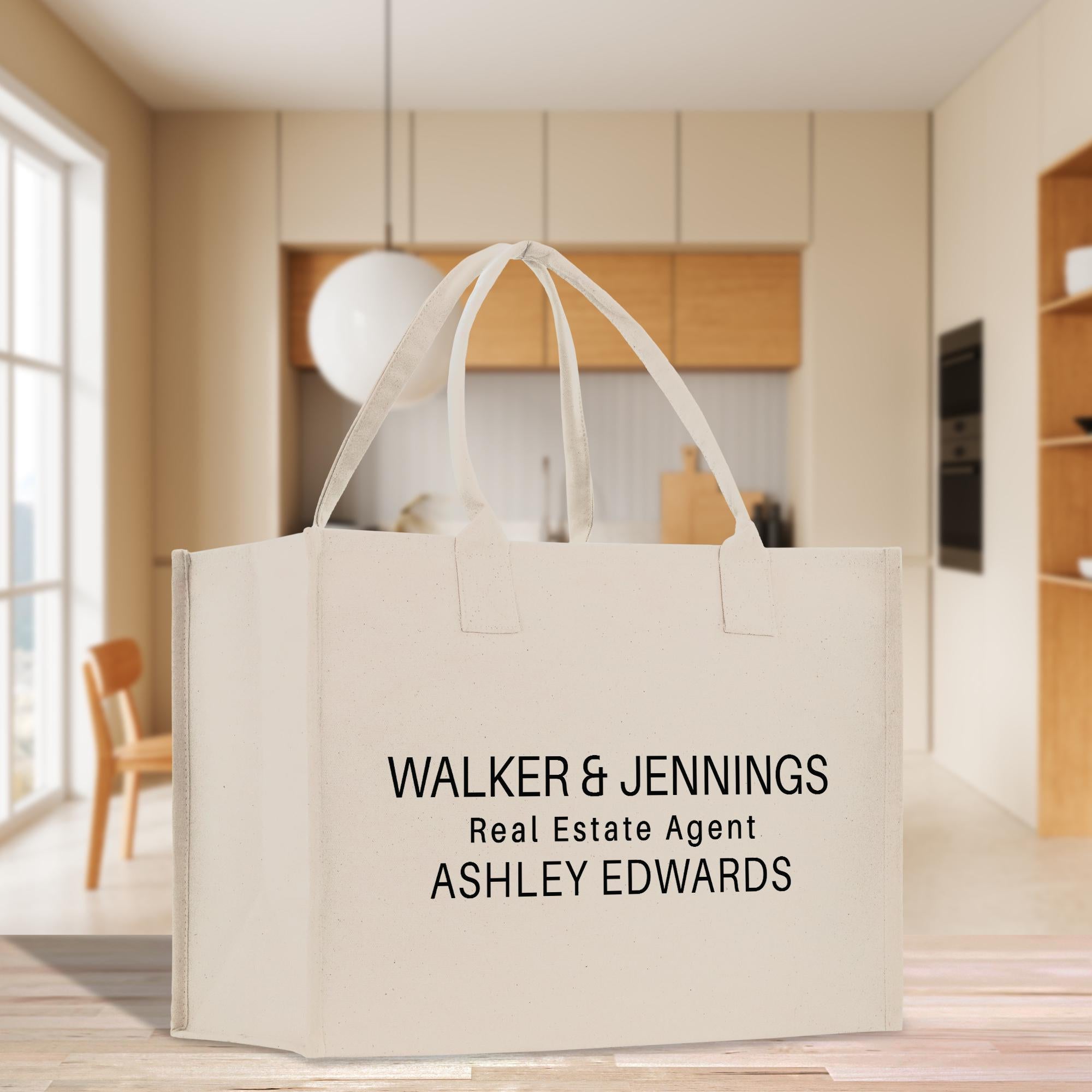 A large white tote bag with text printed on it, placed on a wooden floor in a modern-looking room with a kitchen visible in the background.