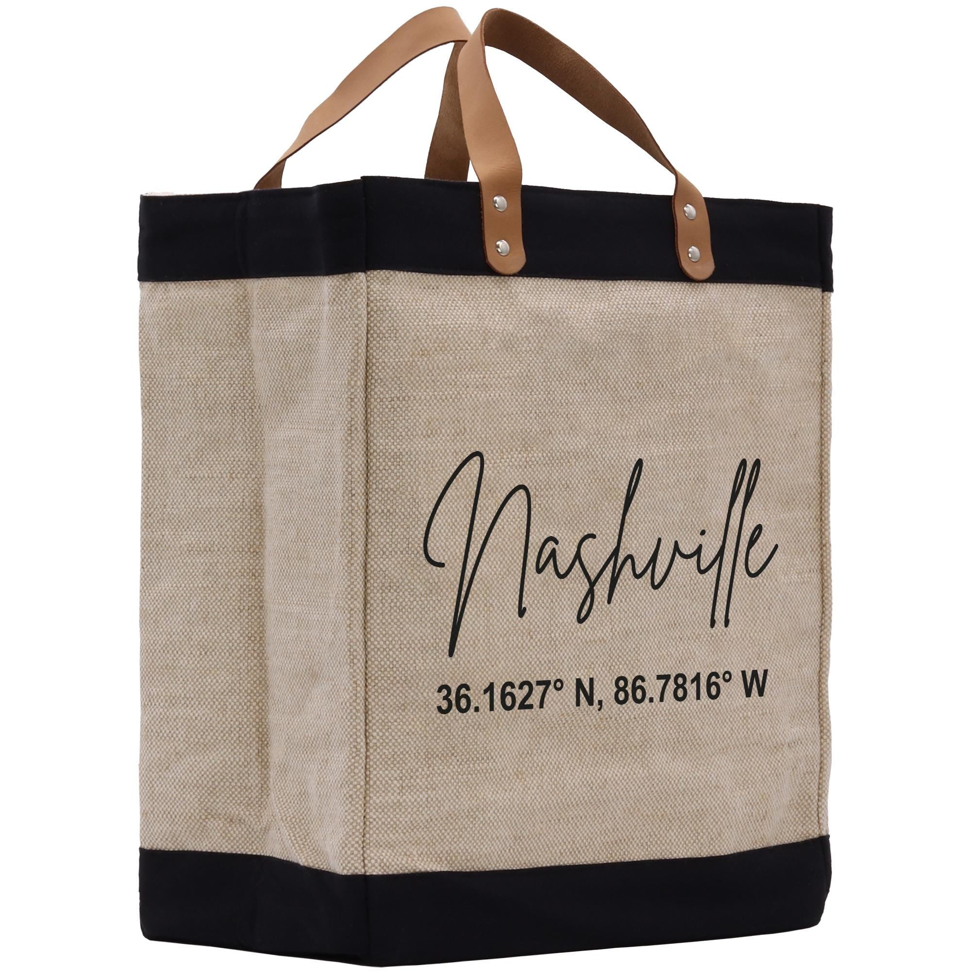 A beige tote bag with black trim and leather handles, featuring the text &quot;Nashville&quot; and a location coordinate printed on it.