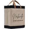 A beige tote bag with black trim and leather handles, featuring the text "Nashville" and a location coordinate printed on it.