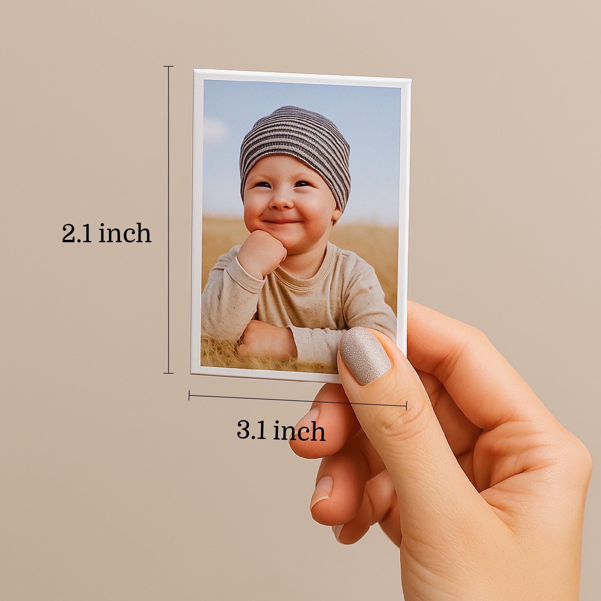 A person&#39;s hand holding a small picture of a smiling baby, with measurements indicating the photo is 2.1 inches in size and 3.1 inches in height.