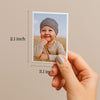 A person's hand holding a small picture of a smiling baby, with measurements indicating the photo is 2.1 inches in size and 3.1 inches in height.