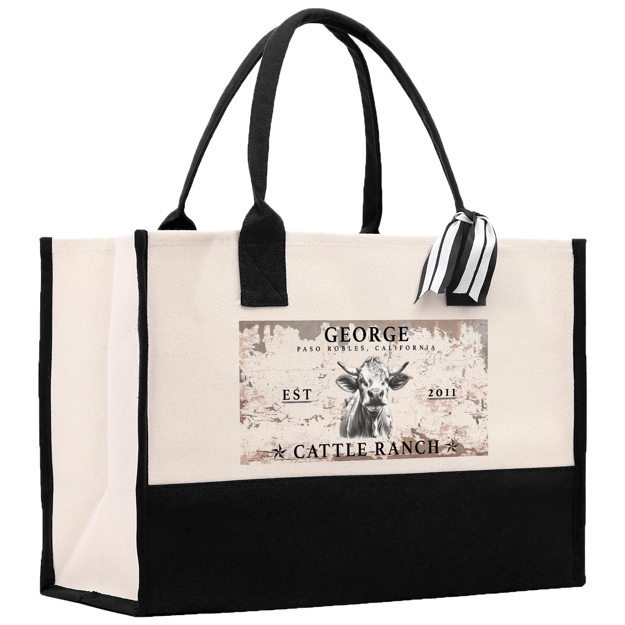 a large tote bag with a black and white design. The bag has a handle and a strap, and it has a label on it that says &quot;GEORGE CATTLE RANCH EST 2011&quot;.