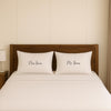 A neatly made bed with two white pillows, each with the name "Mrs Jones" written on it.