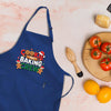 A blue apron with the text "COOKIE BAKING CREW" printed on it, along with various baking-related items such as a wooden whisk, a wooden cutting board with tomatoes, and a lemon.