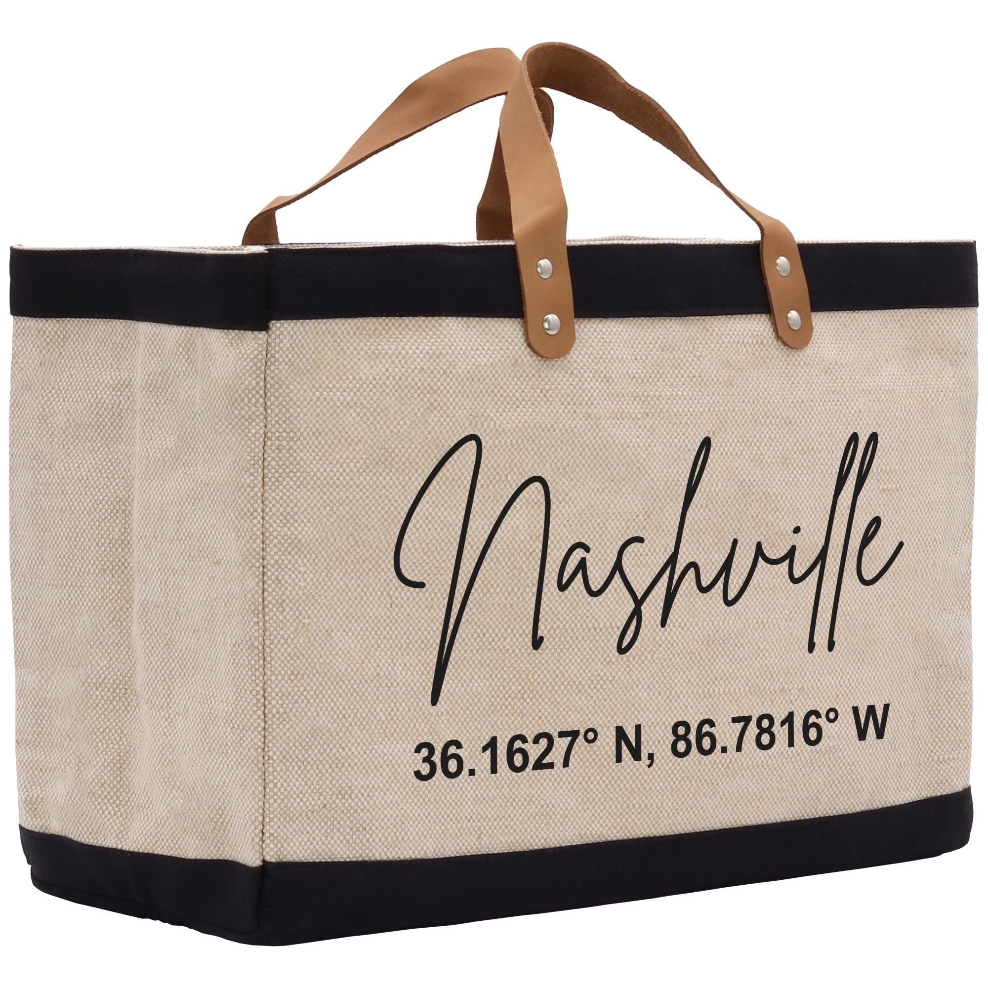 A beige tote bag with black trim and leather handles, featuring the text &quot;Nashville&quot; and a location coordinate.