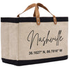 A beige tote bag with black trim and leather handles, featuring the text "Nashville" and a location coordinate.