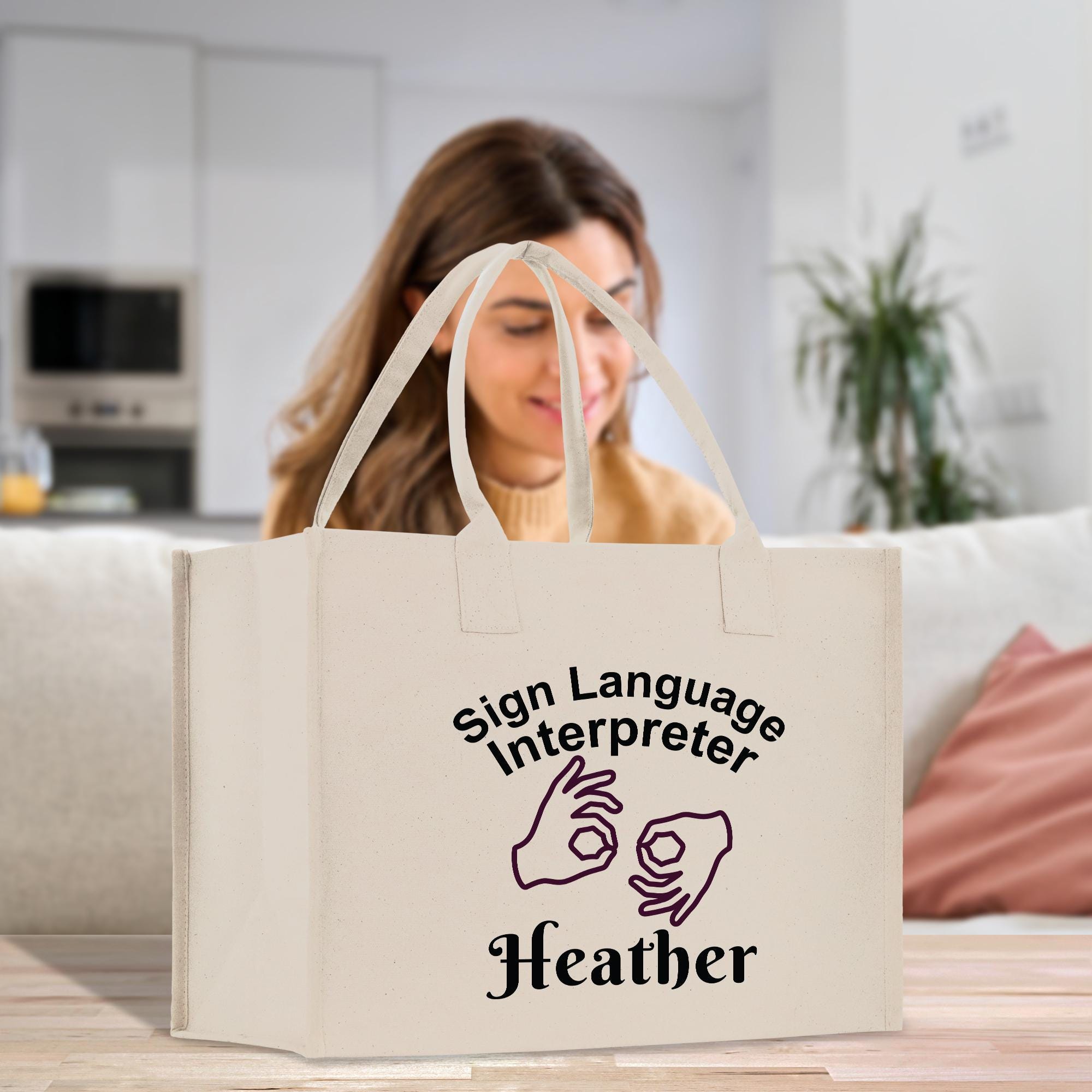 A woman is sitting in a kitchen, looking at a white tote bag with text and hand gestures printed on it.