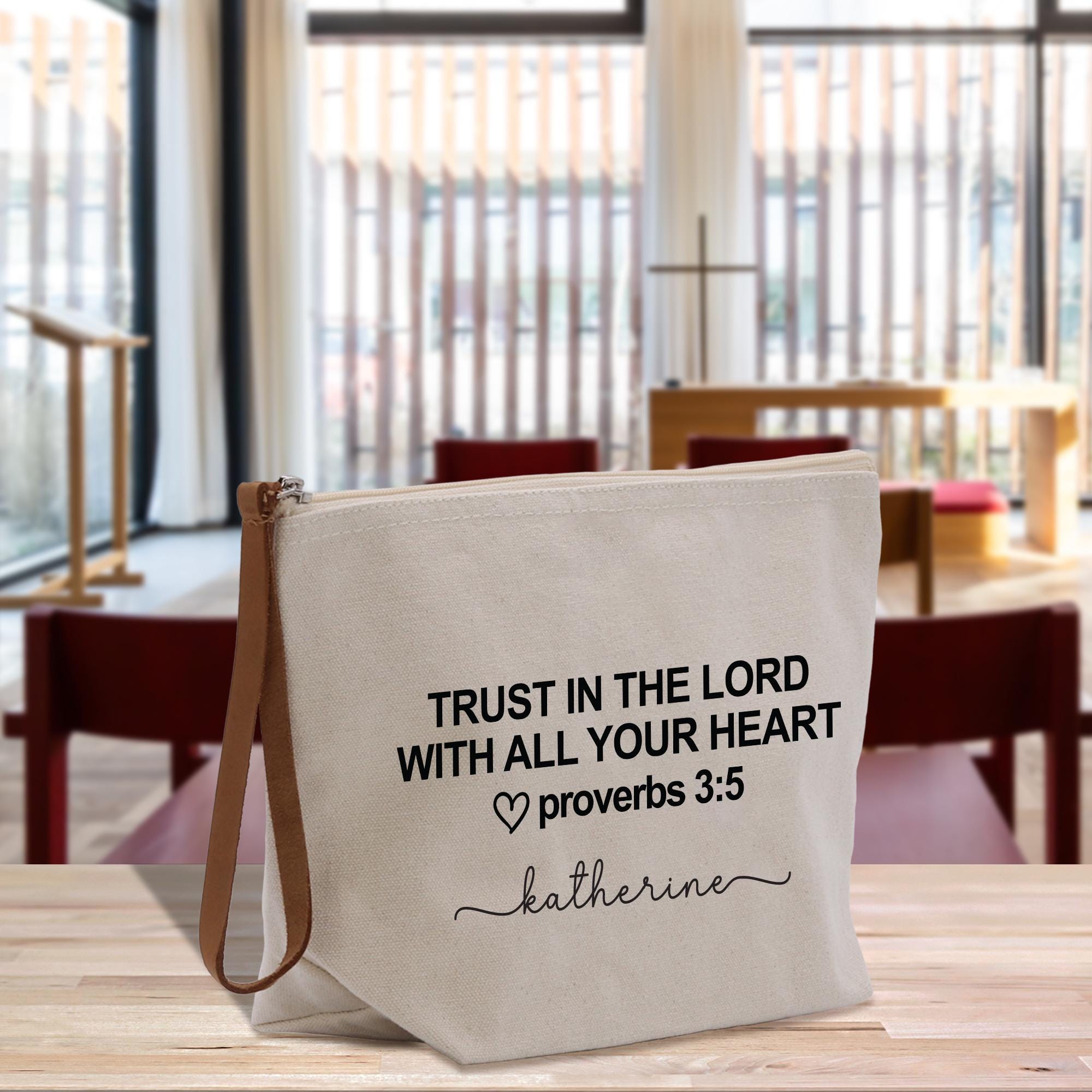 A white canvas tote bag with black text and a leather strap, placed on a wooden surface.