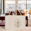 A white tote bag with a circular emblem featuring a cross and floral design, placed on a wooden surface.