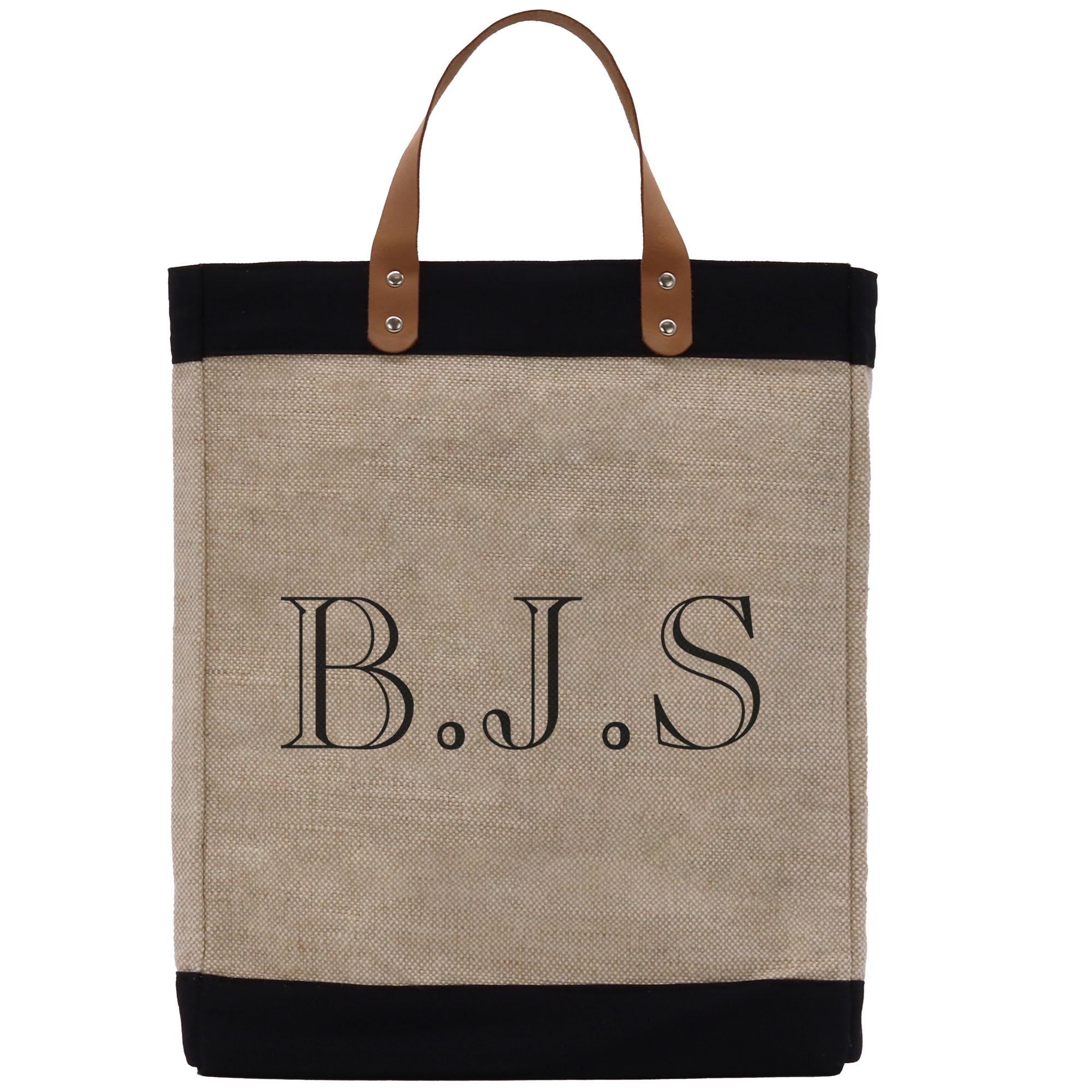 A beige tote bag with black trim and leather handles, featuring the initials &quot;B.J.S.&quot; printed on it.