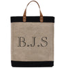 A beige tote bag with black trim and leather handles, featuring the initials "B.J.S." printed on it.