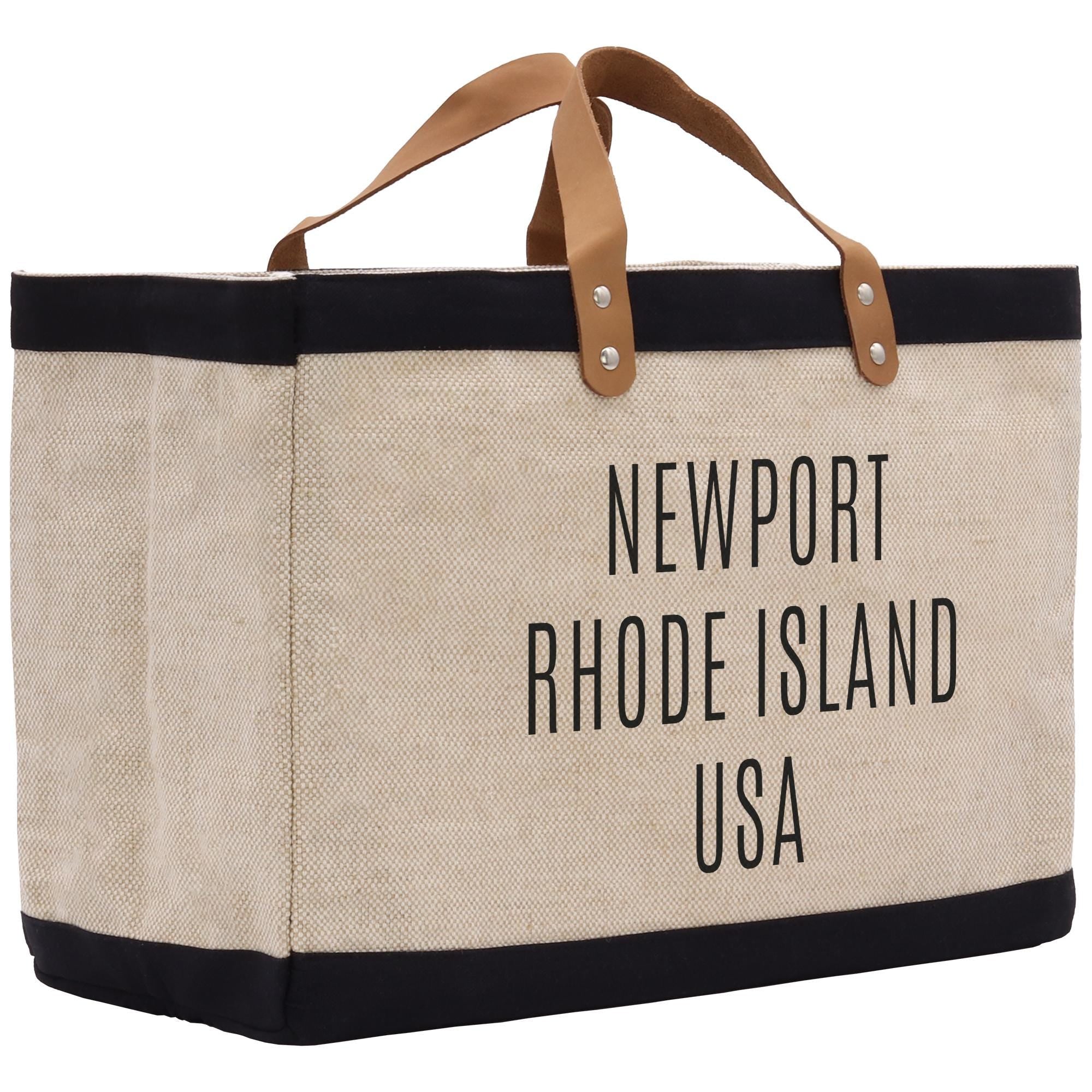 A beige tote bag with black trim and leather handles, featuring the text &quot;NEWPORT RHODE ISLAND USA&quot; printed on it.