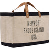 A beige tote bag with black trim and leather handles, featuring the text "NEWPORT RHODE ISLAND USA" printed on it.
