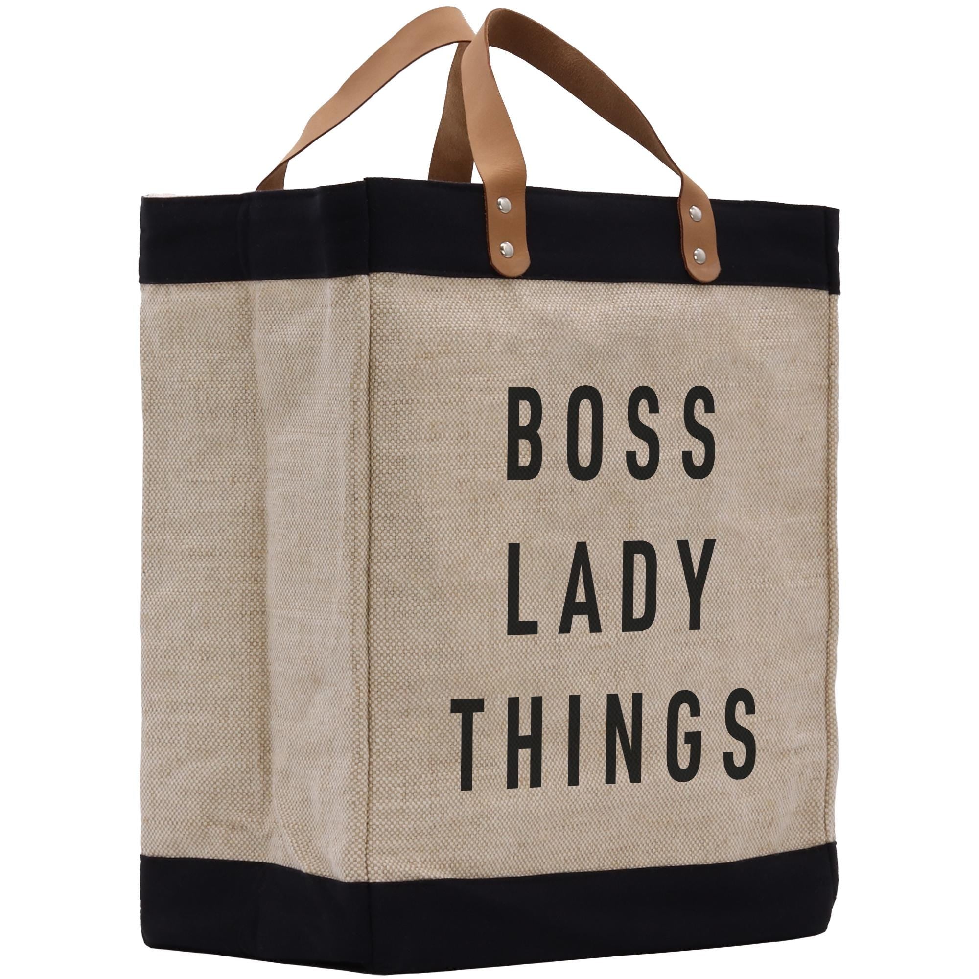 A beige tote bag with black trim and leather handles, featuring the text &quot;BOSS LADY THINGS&quot; printed on it.