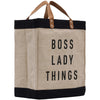 A beige tote bag with black trim and leather handles, featuring the text "BOSS LADY THINGS" printed on it.