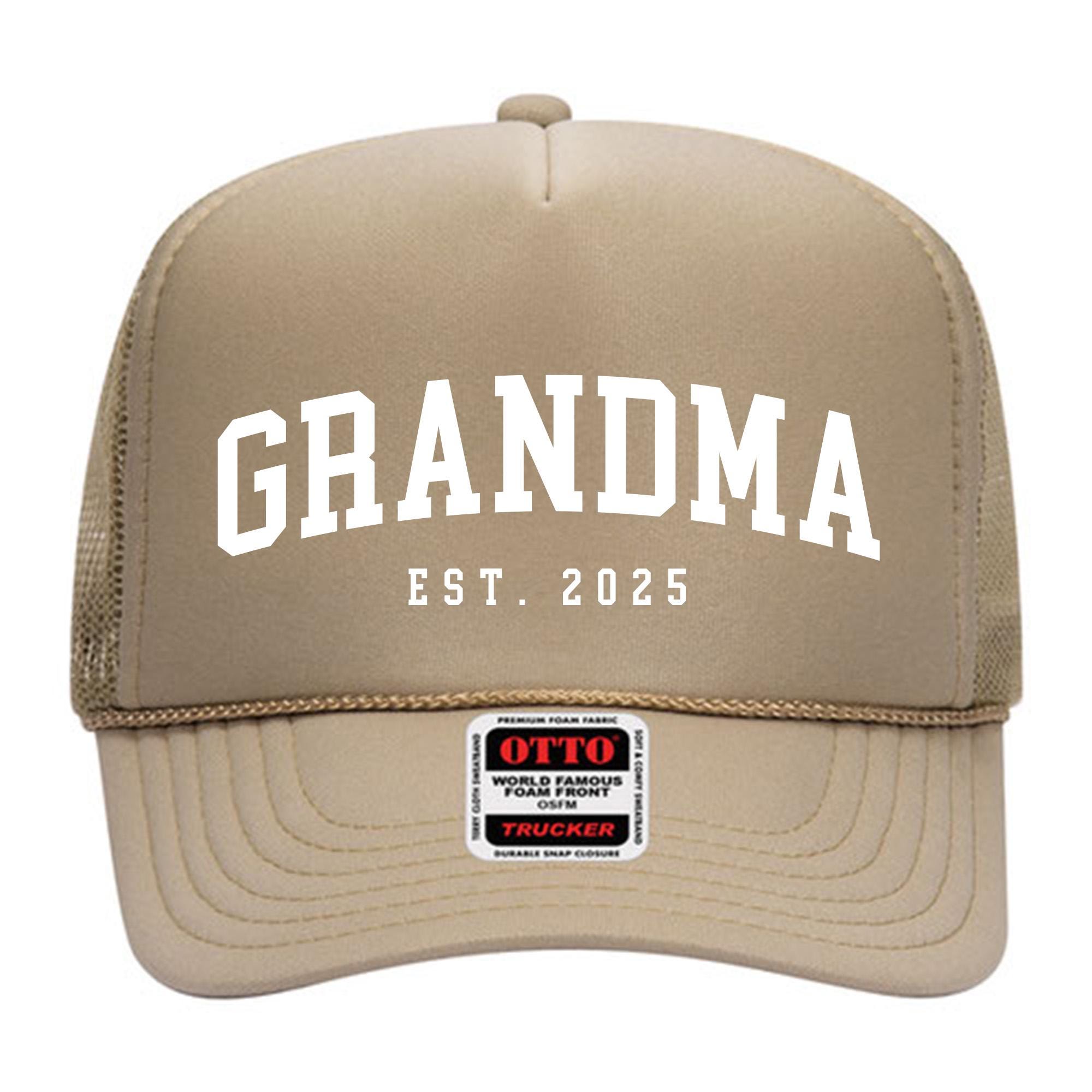 A tan-colored trucker hat with the text &quot;GRANDMA EST. 2025&quot; printed on it.