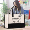 A large tote bag with a sewing kit design printed on it, placed on a wooden surface. In the background, there is a woman who appears to be sewing or working with fabric.