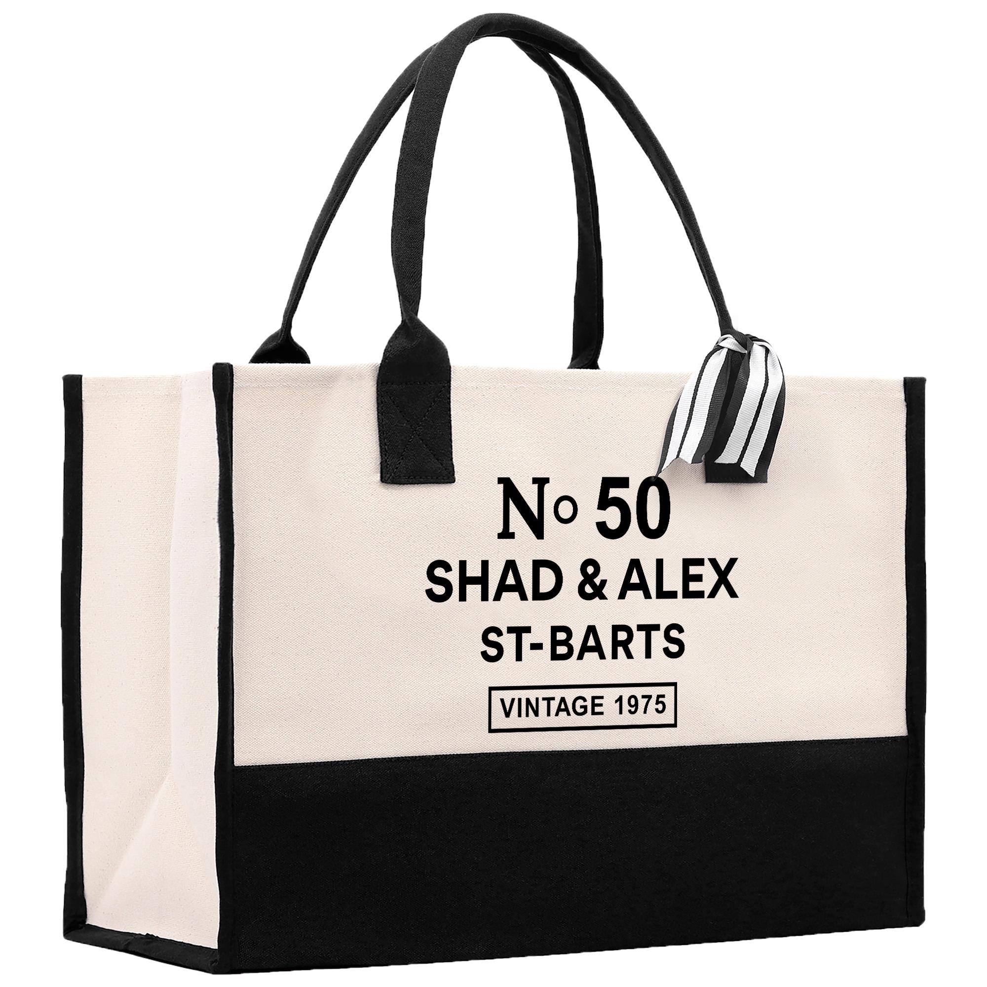 A large tote bag with a black and white color scheme. The bag has a handle and a strap, and it features text that reads &quot;No. 50 SHAD & ALEX ST-BARTS VINTAGE 1975&quot;.