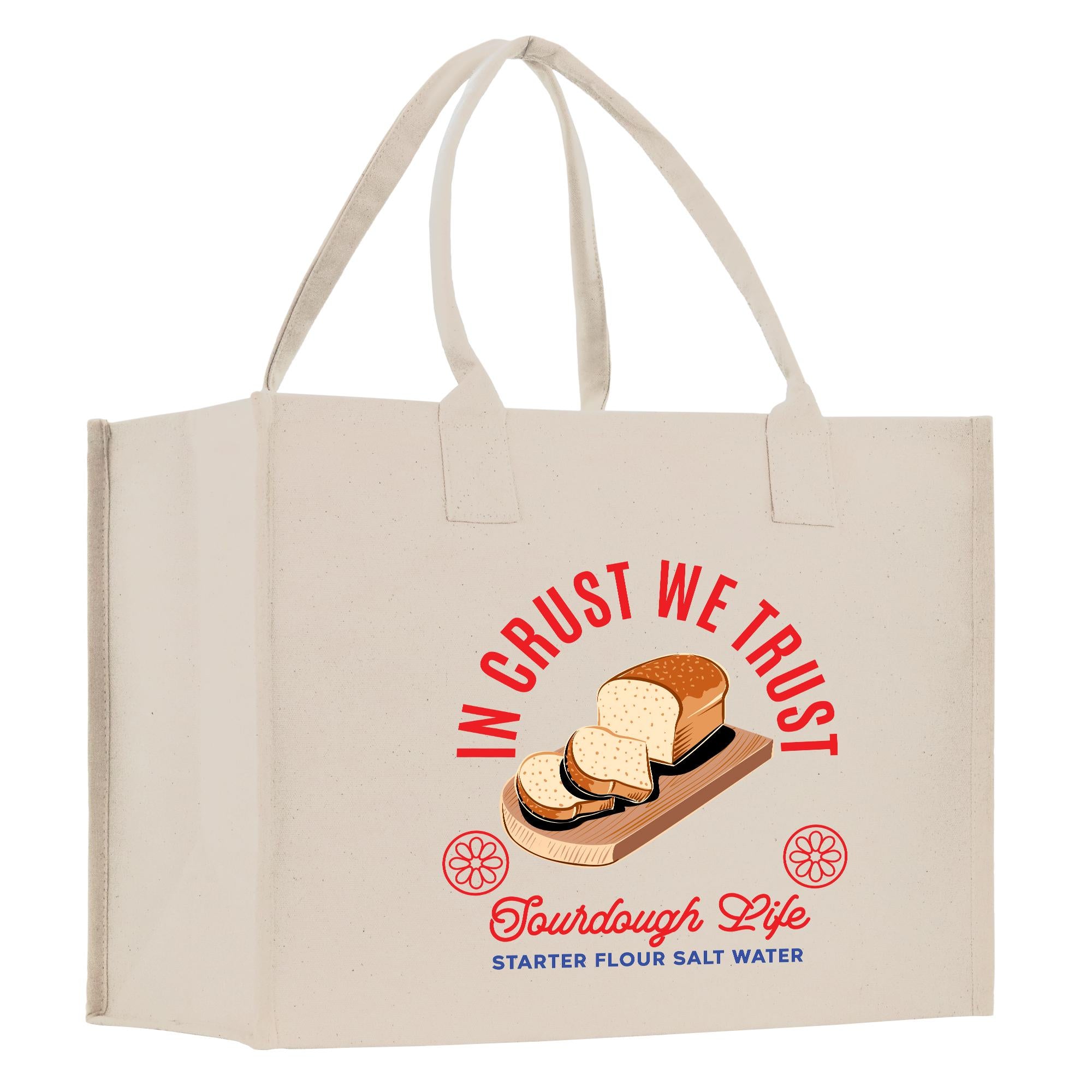 A beige tote bag with a graphic design featuring a loaf of bread and the text &quot;In our crust we trust&quot; and &quot;Tourdough Life starter flour salt water&quot;.