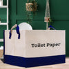 A large white and blue storage container labeled "Toilet Paper" is placed on a wooden floor in a room with green walls and potted plants.