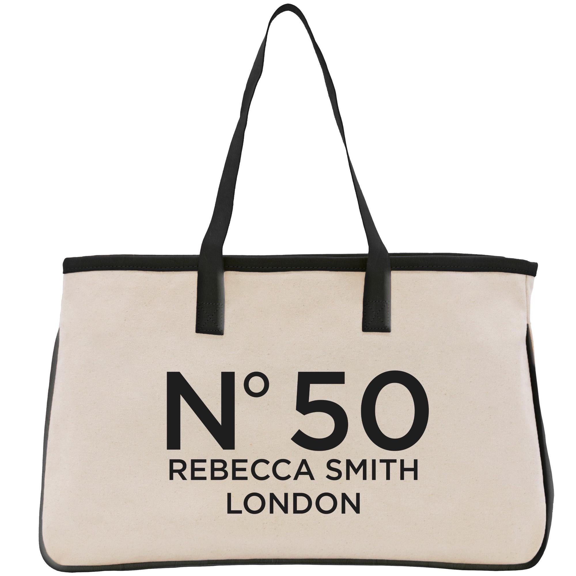 A beige tote bag with black straps and handles, featuring the text &quot;N50 Rebecca Smith London&quot; printed on it.