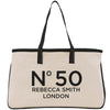 A beige tote bag with black straps and handles, featuring the text "N50 Rebecca Smith London" printed on it.