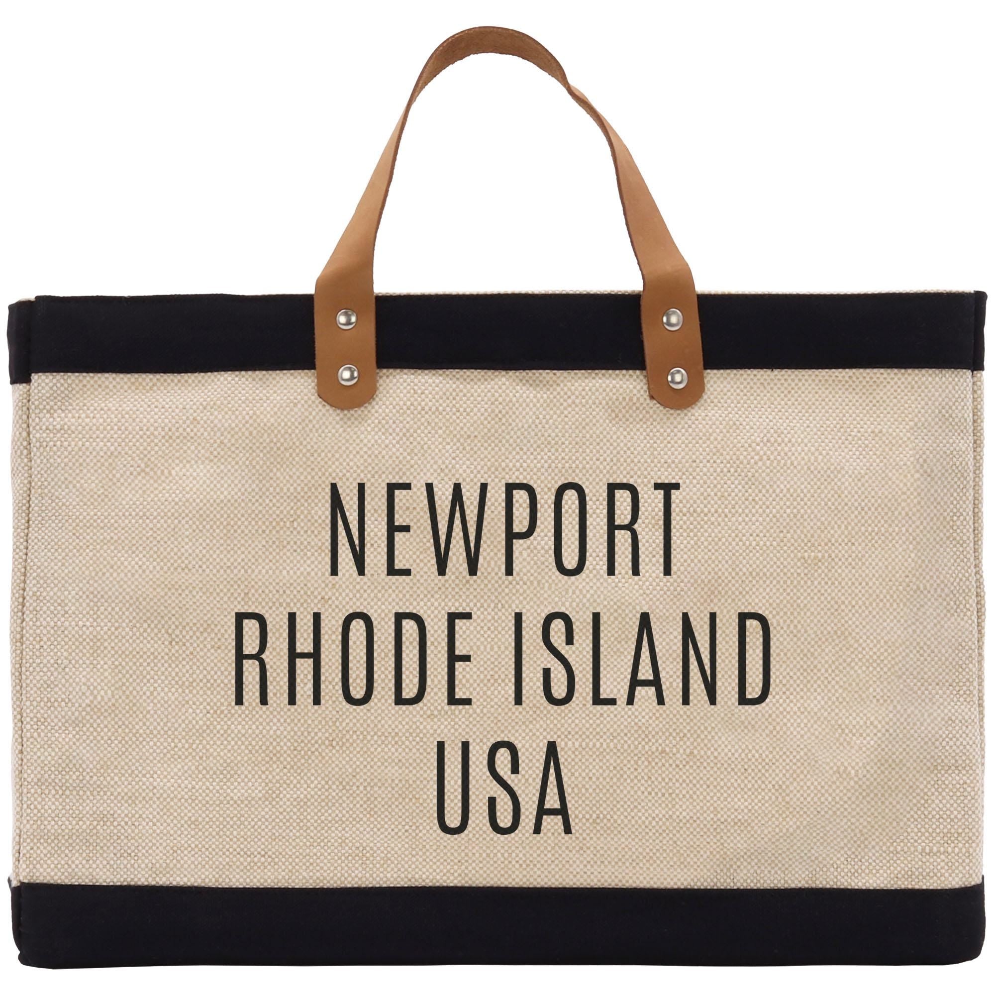 A beige tote bag with black trim and leather handles, featuring the text &quot;NEWPORT RHODE ISLAND USA&quot; printed on it.