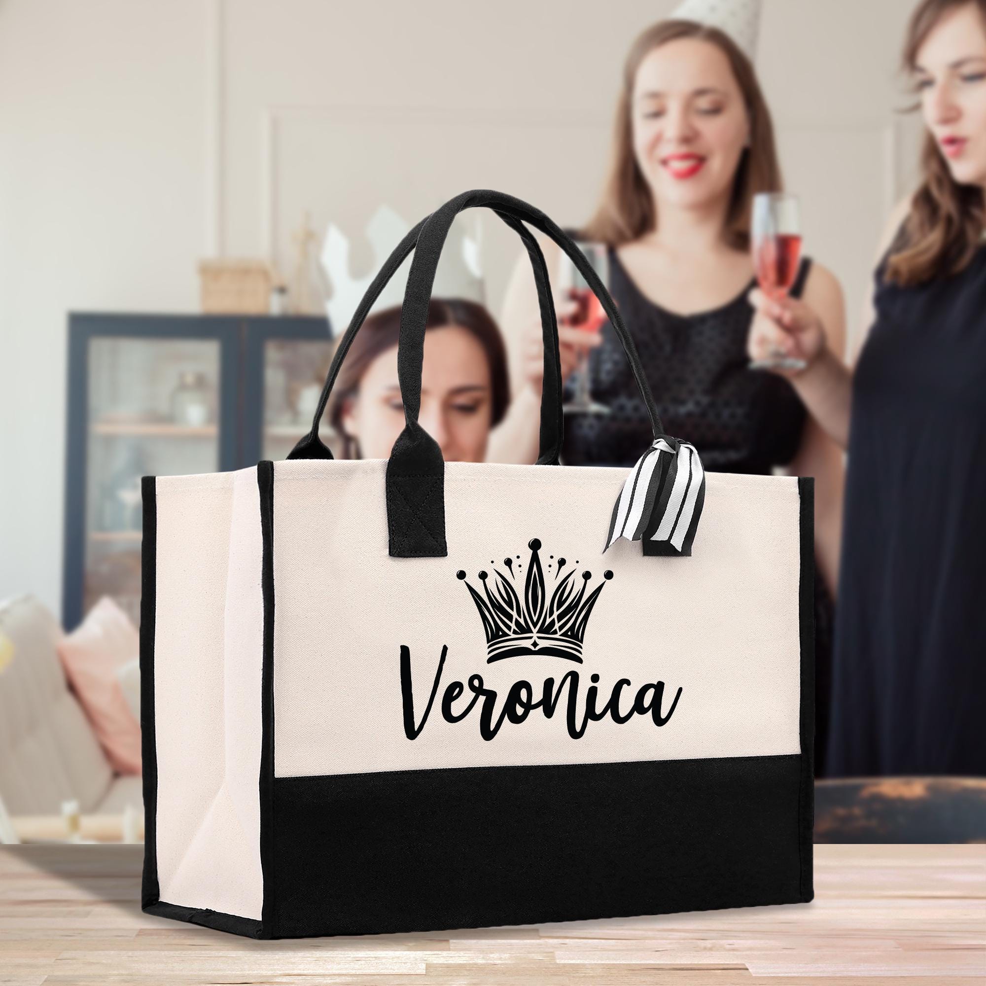 A large tote bag with the name &quot;Veronica&quot; printed on it, placed on a wooden surface. In the background, two women are standing and holding glasses of wine.