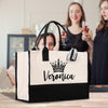 A large tote bag with the name "Veronica" printed on it, placed on a wooden surface. In the background, two women are standing and holding glasses of wine.
